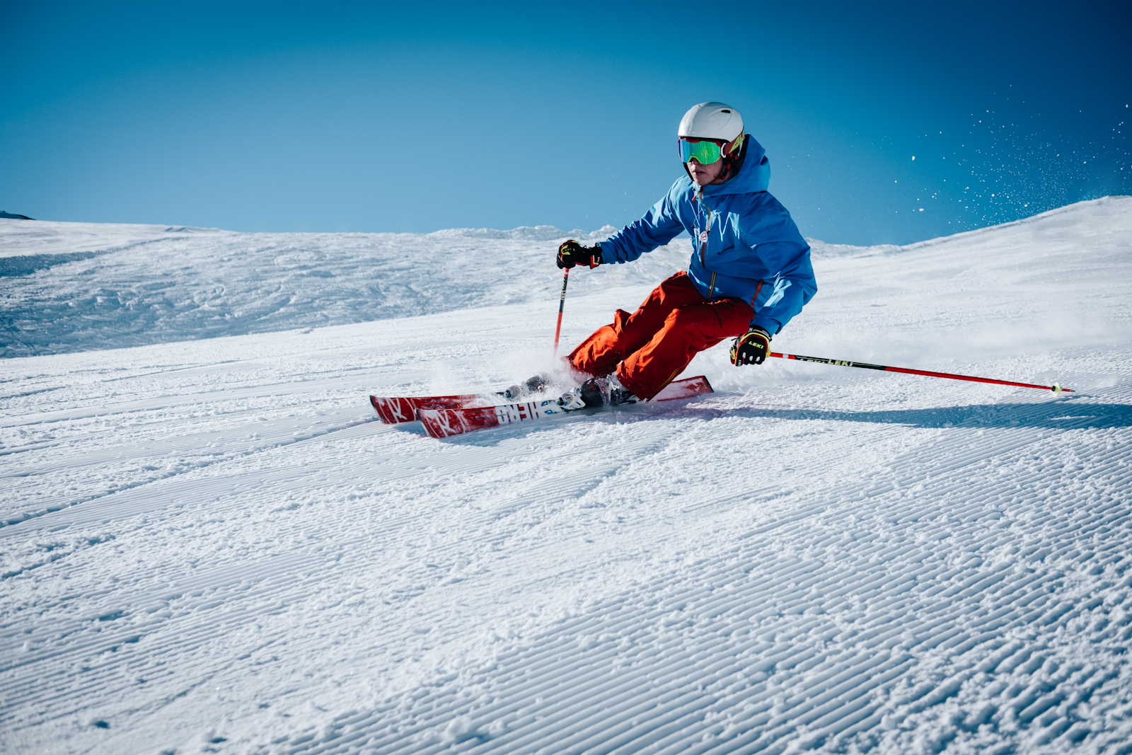 Helicopter landing on pristine snow-covered alpine peak with powder ski tracks curving down the slope